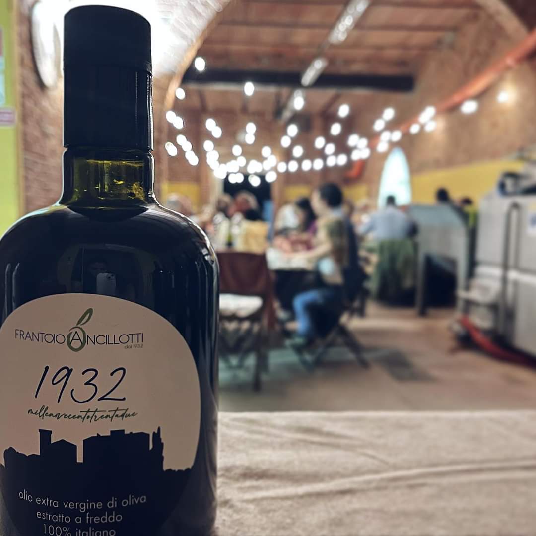 Bottiglia di olio extravergine con la cena dell'olio nuovo sullo sfondo